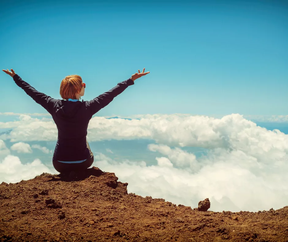 a woman sitting on a mountain with her arms raised