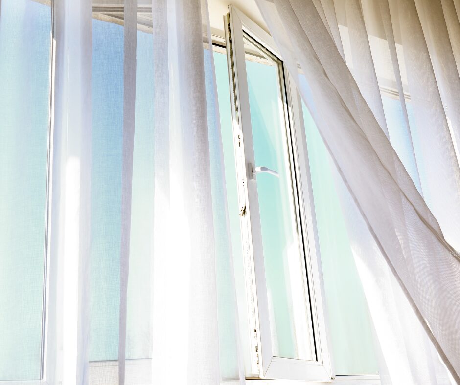 An open window with white curtains flowing in the breeze