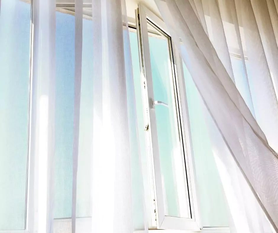 An open window with white curtains flowing in the breeze